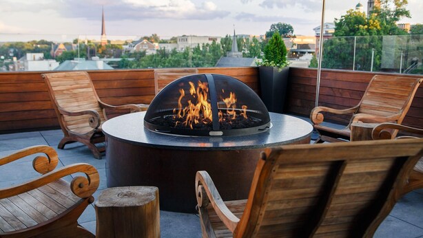A rooftop terrace with a circular fire pit surrounded by wooden chairs and an umbrella. - Sage & Stone cottage-2BR near Downtown Lynchburg & LU (Lynchburg)