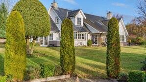 Une grande maison avec une pelouse bien entretenue, des haies taillées avec soin et un ciel dégagé.