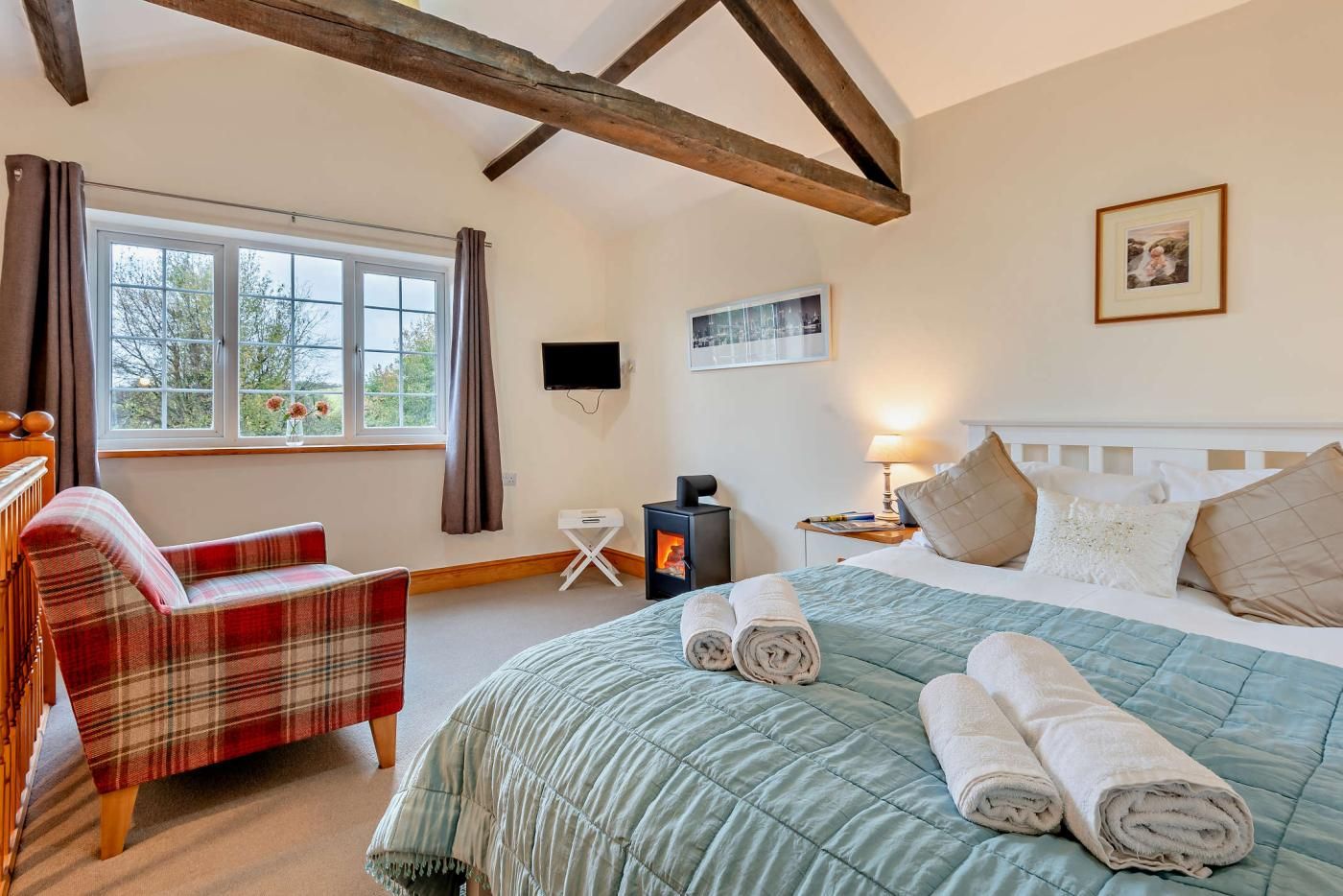 A bedroom with a bed, a chair, a TV, a fireplace, and a window with curtains.