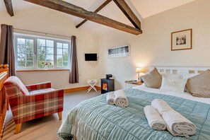 A bedroom with a bed, a chair, a TV, a fireplace, and a window with curtains.