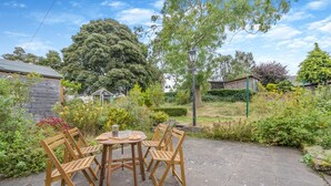 Eine Gartenpatio mit einem runden Tisch und vier Holzstühlen, umgeben von üppigem Grün und Bäumen.