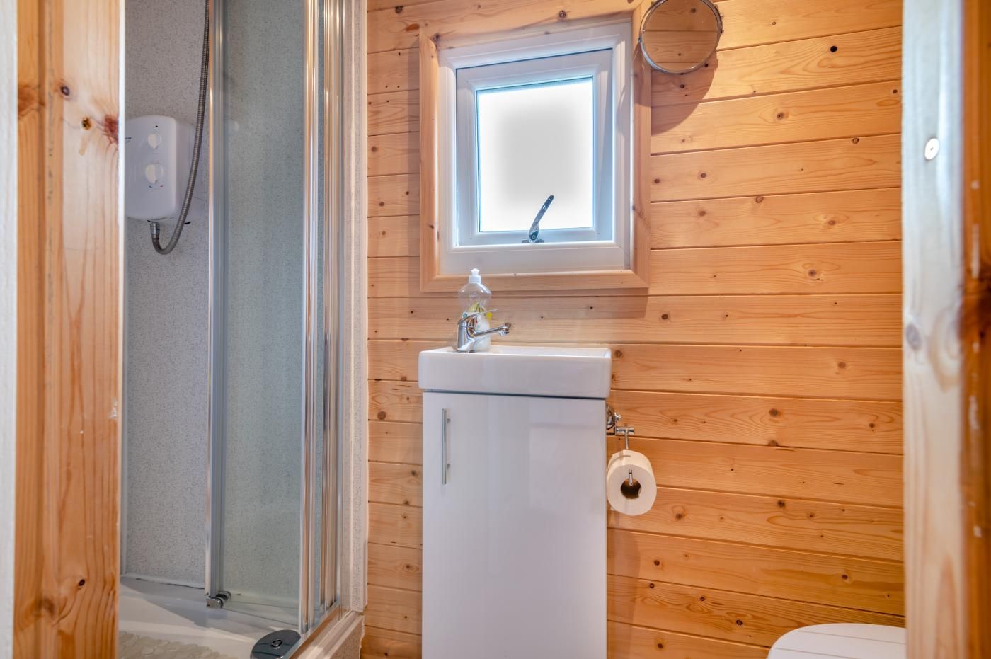 A wooden-paneled bathroom with a shower, a sink, and a toilet.