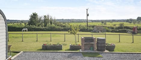 A rural property with a fenced pasture, a white horse, and a stone oven.