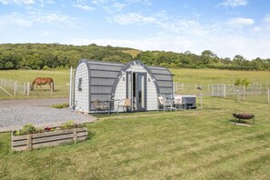 A small, single-story building with a sloped roof, a patio with outdoor seating, and a horse grazing in the background.