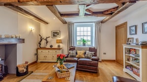 Ein gemütliches Wohnzimmer mit Kamin, Holzbalken, einer Couch, einem Couchtisch und einem Bücherregal.