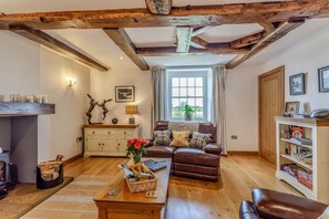 A cozy living room with a fireplace, wooden beams, a sofa, a coffee table, and a bookshelf.