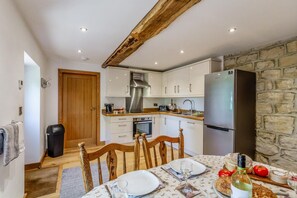 A compact kitchen with white cabinets, a stainless steel range hood, a built-in oven, and a large refrigerator.