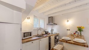 A compact kitchen with white cabinets, a microwave, a stove, and a sink. There is a window with blinds, a stool, and a vase with flowers on the counter. - 1 Bed in Whitby (oc-e29968) (Egton Bridge)