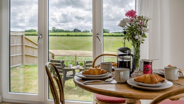 Una mesa de desayuno con cruasanes, una cafetera y un frasco de mermelada, con vistas a un campo cubierto de hierba y una cerca de madera.
