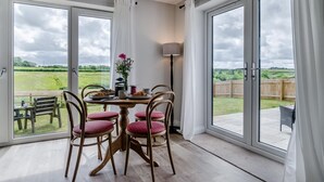 Comedor con una mesa lista para cuatro personas, una lámpara y vistas a un campo verde a través de amplios ventanales.