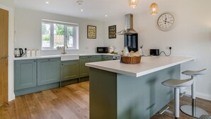 Cocina moderna con armarios verde claro, una isla blanca e iluminación colgante.