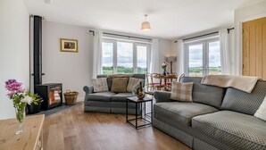 Una sala de estar acogedora con chimenea, un conjunto de sofás, una mesa de comedor y ventanas amplias que ofrecen vistas al exterior.