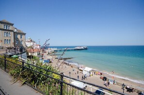 Una passeggiata costiera con un molo che si protende verso il mare, una passeggiata con panchine e persone, e edifici lungo il lungomare.