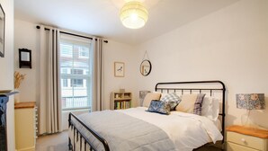 Un dormitorio con cama, mesitas de noche, una estantería y una ventana con cortinas.