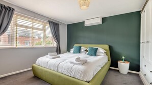 Um quarto com uma cama, janela com cortinas, abajur e cômoda.