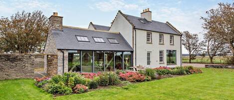 A two-story house with a stone wall, a glass conservatory, and a well-maintained garden.