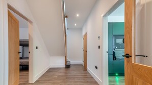 A hallway with wooden flooring, white walls, and doors leading to different rooms. - 4 Bed in Berwick-upon-Tweed (oc-h29940) (Cheswick Buildings)