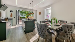 A modern kitchen with a central island, dining area with grey upholstered chairs, and a view of the outdoors. - 4 Bed in Berwick-upon-Tweed (oc-h29940) (Cheswick Buildings)