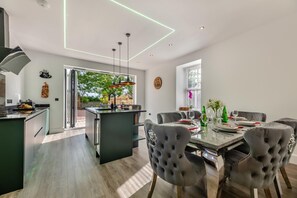 A modern kitchen with a central island, a dining area with a glass table, and a view of the outdoors. - 4 Bed in Berwick-upon-Tweed (oc-h29940) (Cheswick Buildings)