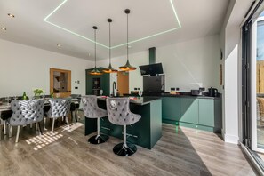 A modern kitchen with a central island, bar stools, pendant lighting, and a view through a glass door. - 4 Bed in Berwick-upon-Tweed (oc-h29940) (Cheswick Buildings)