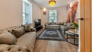 A living room with a sectional sofa, a smaller sofa, a coffee table, a TV, and a large bull mural on the wall. - 4 Bed in Berwick-upon-Tweed (oc-h29940) (Cheswick Buildings)