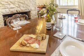 A wooden dining table with a wooden board holding sliced salami, cheese, and bread. There are wine glasses and a bottle of wine on the table. - 4 Bed in Swanage (oc-m29981) (Swanage)