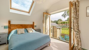Quarto com uma cama grande, claraboia, varanda com vista para o jardim e porta de vidro deslizante.