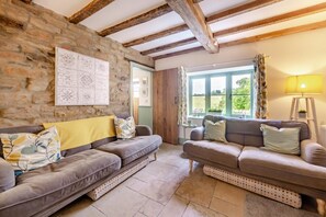 A cozy living room with two sofas, a stone wall, wooden beams, a large window with curtains, and a floor lamp. - 3 Bed in Lea (oc-c29996) (Lea)
