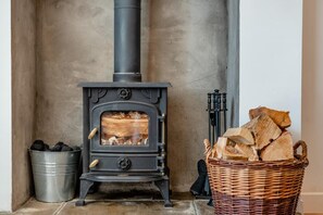Een houtkachel met een metalen emmer haardhout en een rieten mand vol blokken.