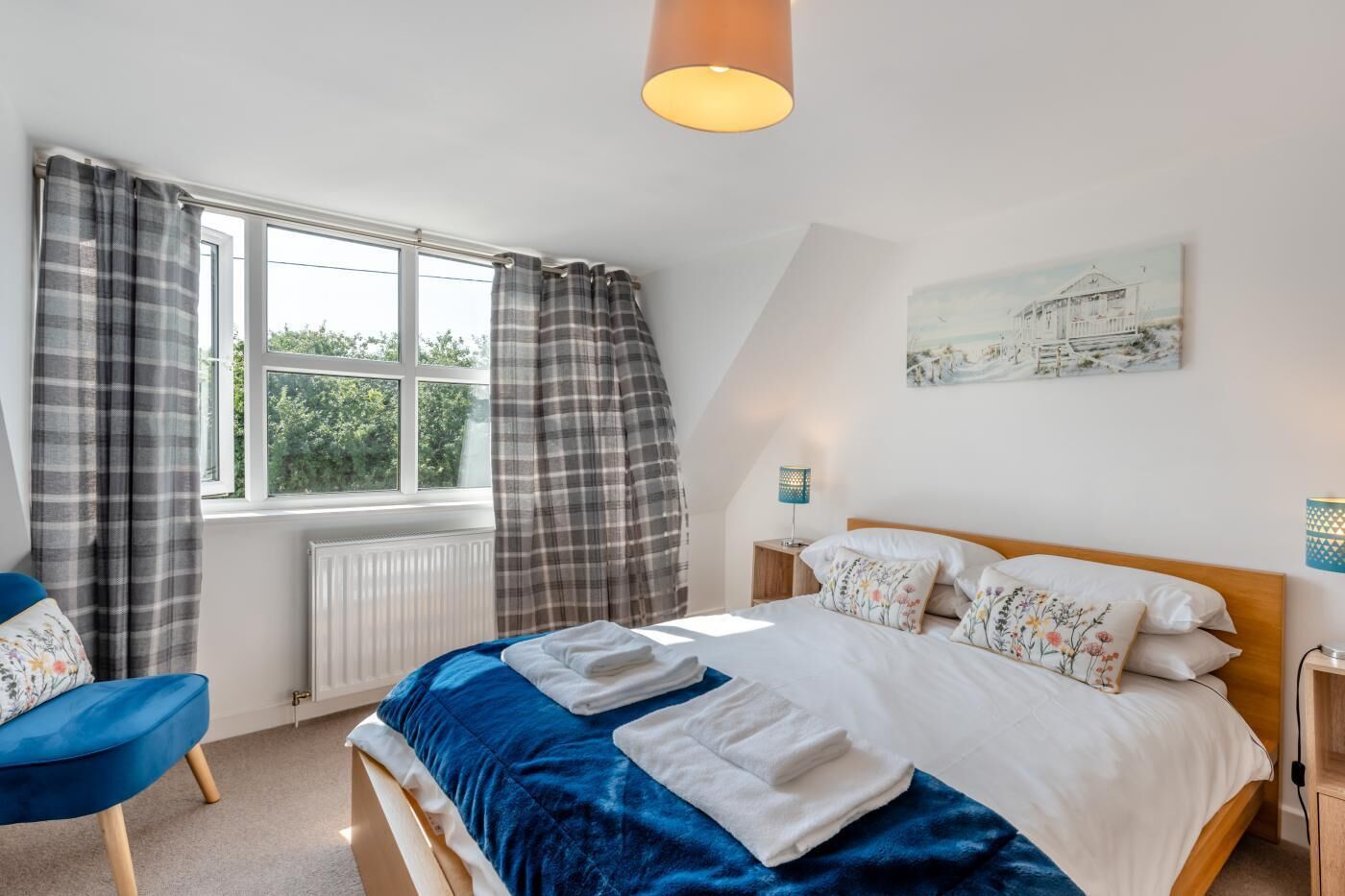 A bedroom with a bed, a chair, a window with curtains, a radiator, a lamp, and a painting on the wall.