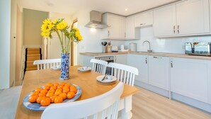 A modern kitchen with white cabinets, a wooden dining table, and a vase with yellow flowers. - 2 Bed in Tayport (oc-w30005) (Dundee)