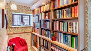 Una biblioteca con estanterías llenas de libros, una ventana con vistas y un sillón rojo.