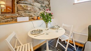 A dining area with a stone wall, white chairs, a round table with plates and glasses, and a vase with flowers.