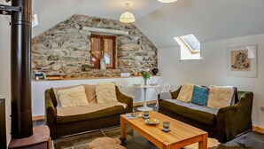 A cozy living room with two sofas, a wooden coffee table, and a stone wall.