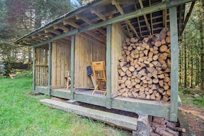 A wooden cabin with a porch, a stack of firewood, and a chair. - 1 Bed in Brithdir (oc-w30045) (Brithdir and Llanfachreth)