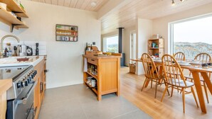 A modern kitchen with wooden cabinets, a built-in oven, and a dining area with wooden chairs and a table. - 2 Bed in Lochinver (oc-t30029) (Clachtoll)