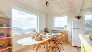 A dining area with a wooden table set for four, surrounded by chairs, with a view of the city through large windows. - 2 Bed in Lochinver (oc-t30029) (Clachtoll)