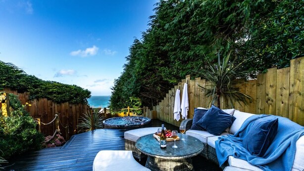 Eine Terrasse mit Holzboden, einem Korbus-Sofa mit Kissen, einem runden Tisch und einem Whirlpool.
