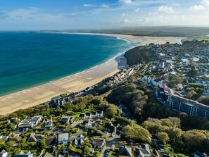 An aerial view of a coastal residential area with houses, a beach, and a lighthouse in the distance. - 4 Bed in Carbis Bay (oc-m30075) (Carbis Bay)