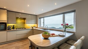 Eine moderne Küche mit einer großen Kochinsel, einem Einbauofen und Meerblick durch ein großes Fenster.