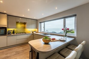 Eine moderne Küche mit einer großen Kochinsel, einem Einbauofen und Meerblick durch ein großes Fenster.