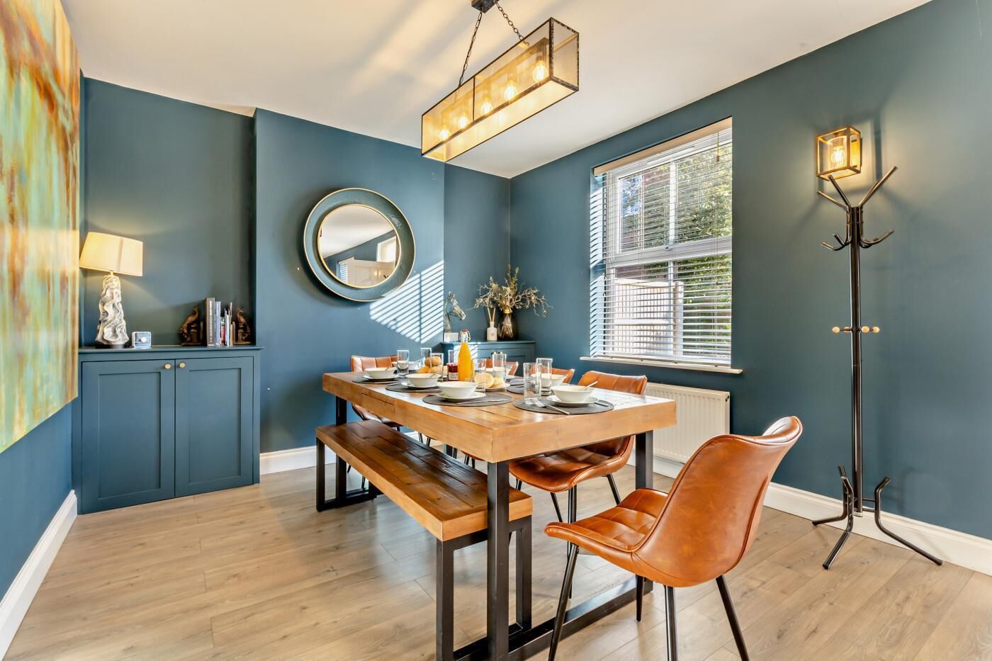 A dining area with a wooden table, brown leather chairs, a round mirror, and a pendant light.