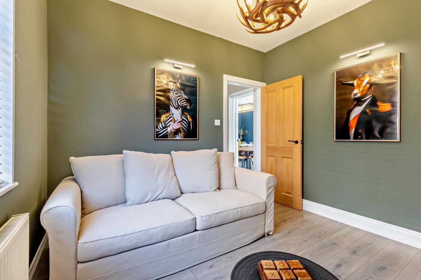 A living room with a beige sofa, a wooden door, and two framed artworks on the wall.