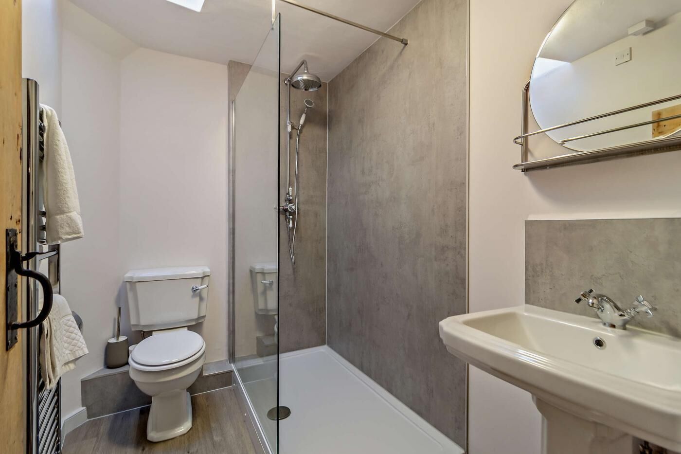 Een moderne badkamer met een douche met glazen wand, een wit toilet en een wastafel met een spiegel erboven.