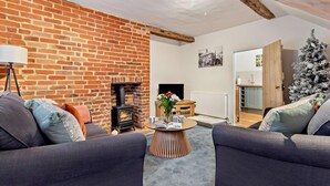 A cozy living room with a brick fireplace, two sofas, a coffee table, and a Christmas tree. - 2 Bed in Lavenham (oc-t30056) (Lavenham)
