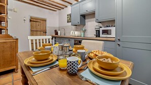 A breakfast setup with bowls, mugs, and a croissant on a wooden table in a kitchen with grey cabinets and a wooden ceiling. - 2 Bed in Lavenham (oc-t30056) (Lavenham)