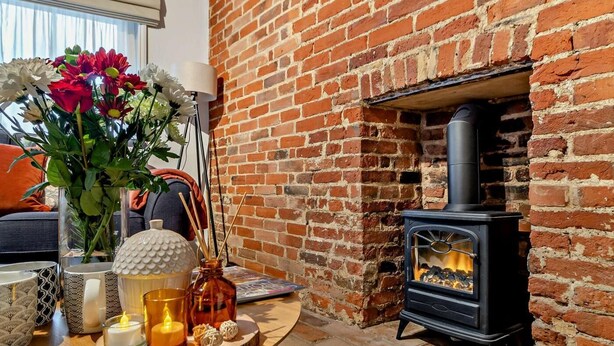A cozy room with a brick fireplace, a table with candles, and a vase of flowers. - 2 Bed in Lavenham (oc-t30056) (Lavenham)