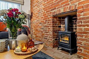 A cozy room with a brick fireplace, a table with candles, and a vase of flowers. - 2 Bed in Lavenham (oc-t30056) (Lavenham)