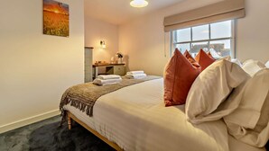 A hotel room with a large bed, a desk, a chair, a window with a view, and a painting on the wall. - 2 Bed in Lavenham (oc-t30056) (Lavenham)