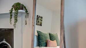 Un dormitorio con una cama, almohadas verdes y rosas, una planta en la pared y una colección de cuadros enmarcados.